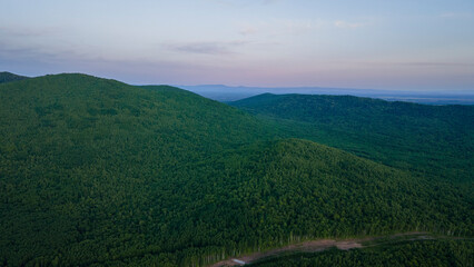 Aerial view of the country road and power lines near to the mountain range, coniferous high forest and the river at summer cloud evening with yellow horizon, color