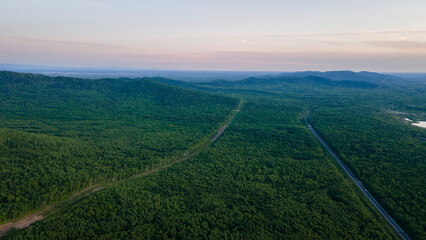 Aerial view of the country road and power lines near to the mountain range, coniferous high forest and the river at summer cloud evening with horizon, orange color