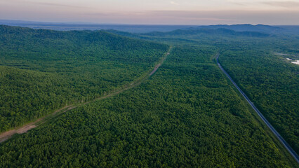 Aerial view of the country road and power lines near to the mountain range, coniferous high forest and the river at summer cloud evening with horizon, yellow color