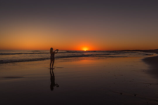 Woman taking photos of the sunset on the beach.