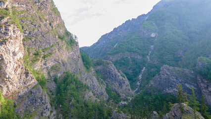 Aerial view of the mountain river in the valley of the rocky mountain ridges, on which snow lies in places at summer cloud morning, orange color of the photo