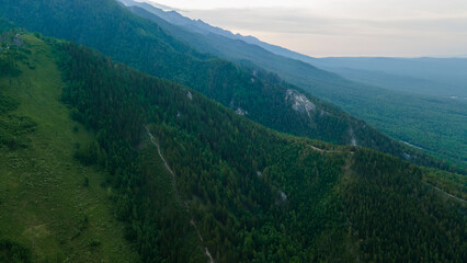 Obraz premium Aerial view of a high valley of the rocky mountain range, on which snow lies in places, near to the fast mountain river at summer cloud morning, blue image