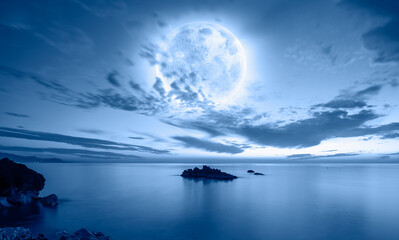 Night sky with blue moon in the clouds - Rocky coastline with power sea wave "Elements of this image furnished by NASA