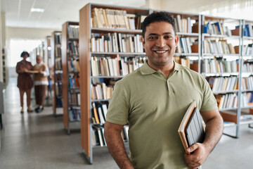 Portrait of adult student smiling at camera while standing in the library - obrazy, fototapety, plakaty