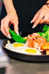 woman chef hand cooking fried eggs with ham, salad and hummus