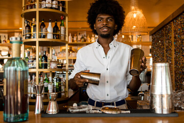 young and happy latin bartender with curly hair starting to prepare a cocktail