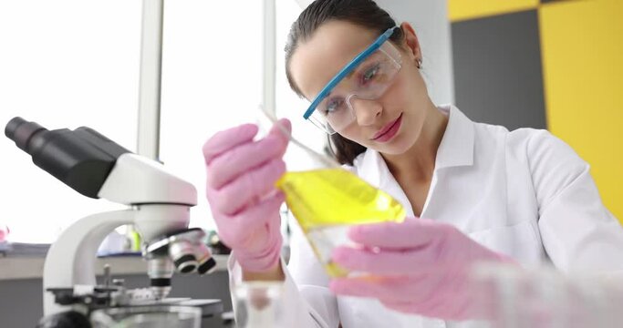 Woman scientist holding yellow glass flask with yellow oily liquid. Testing and education of chemical products concept