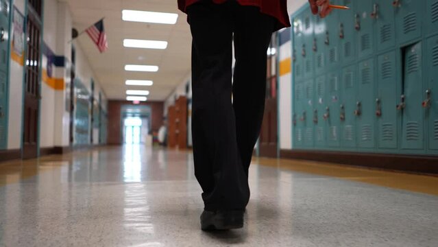 Low angle slow motion of teachers shoes walking down an empty school hallway with US flag in the distance.
