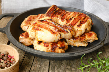 Grilled chicken thigh fillet steak on a wooden table in a cast iron pan.