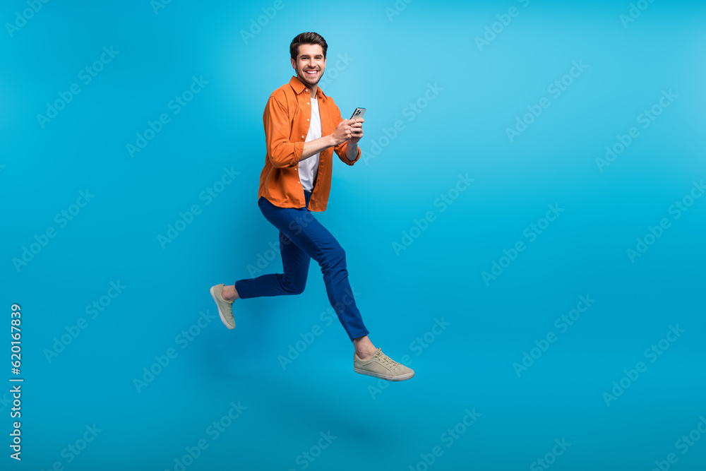 Poster full length profile portrait of handsome excited guy use smart phone jumping rush empty space isolat