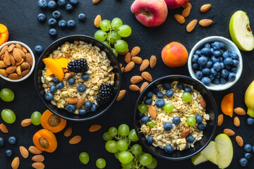Two healthy breakfast bowl with ingredients granola fruits greek yogurt and berries on dark...