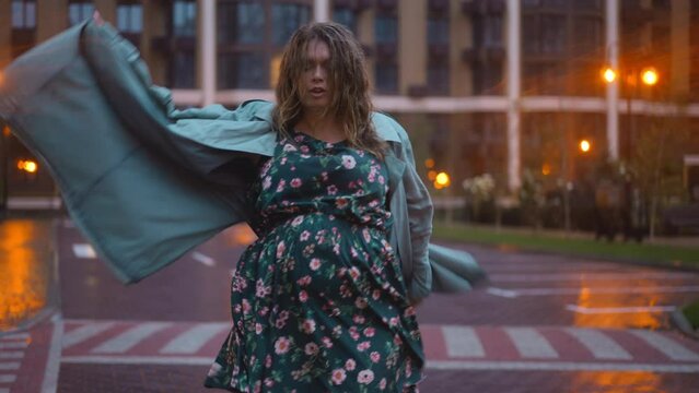 Self confident plus-size woman dancing in slow motion on urban city street in twilight. Portrait of joyful Caucasian lady having fun on rainy evening in dusk outdoors