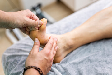 An unrecognizable podiatrist is checking an athlete's foot in a modern clinic. Concept of foot...