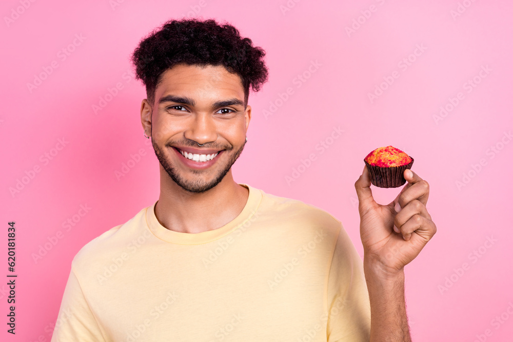 Poster portrait of good mood toothy beaming man afro hairstyle dressed yellow t-shirt hand hold tasty muffi