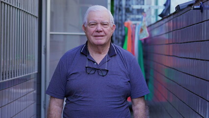 One older man standing in residence outside looking at camera. Portrait of a caucasian elderly male person in 70s, neutral expression