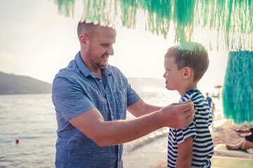 Father helping his son put his clothes on. Father and son having fun on the beach during the day.