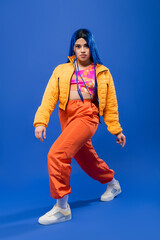 full length, fashion forward, young female model with blue hair posing in puffer jacket and orange...