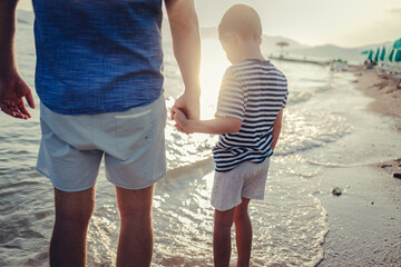 Cropped shot of a Caucasian father and son walking on the beach. Shot of a happy little boy enjoying a day a the beach with his father.