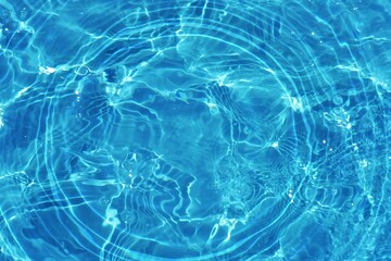 Blue water with ripples on the surface. Defocus blurred transparent blue colored clear calm water surface texture with splashes and bubbles. Water waves with shining pattern texture background.