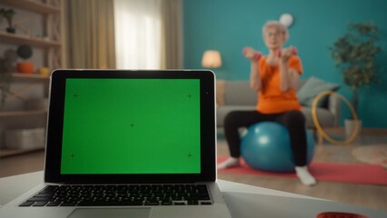 A laptop with a green screen on a table on a blurred background in the living room close up. An...