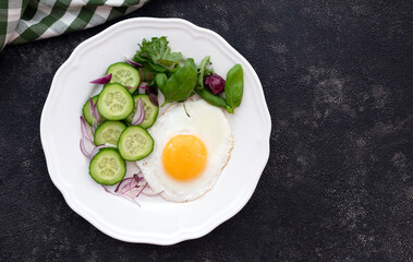 fried eggs on a white plate with cucumbers and green salad