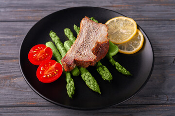 Grilled ribs with green asparagus, tomatoes and lemon on a plate