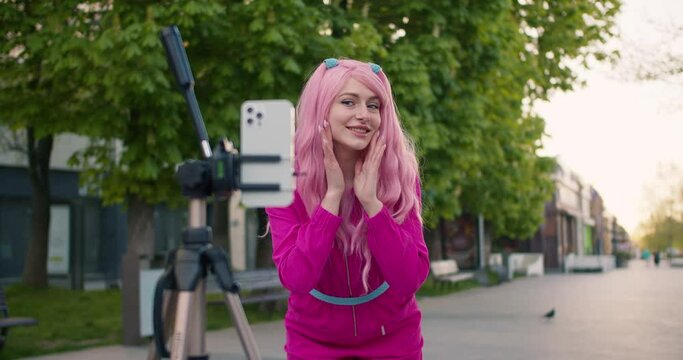 A beautiful girl in pink shoots a video about her appearance on a phone that stands on a tripod. Manifestation of oneself and one's personality, self-affirmation