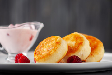 Cottage cheese fritters or syrniki served with yogurt and raspberries, side view.