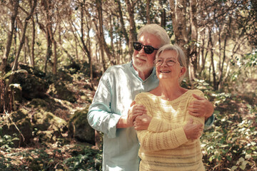 Smiling senior family couple hugging enjoying mountain hike in the woods appreciating nature and freedom, retired seniors man and woman and healthy lifestyle concept