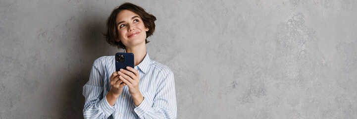 Young brunette woman smiling and using mobile phone