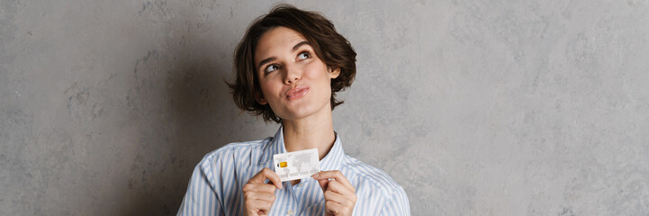 Young brunette woman looking upward while posing with credit card