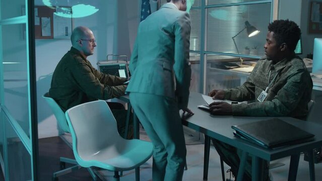 Medium shot of female Caucasian civil officer bringing secret documents to briefing and two multiethnic military colleagues reading them