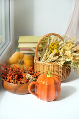 Autumn background. Pumpkin shape cup, pumpkin, books, dry grass in basket on windowsill. symbol of fall season. home cozy composition for Halloween, Thanksgiving holiday. 