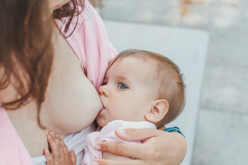 close-up baby sucking mom's breasts outdoors in the park, the concept of breastfeeding and...