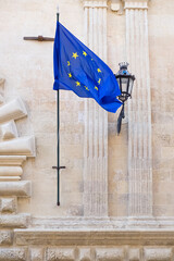European flag displayed outside a Baroque-style institutional building, a lantern on the side.