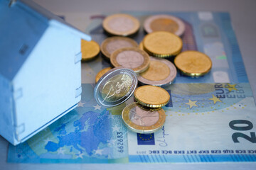 Euro coins resting on banknotes, close up partial view of small wooden house, concept of 'real...