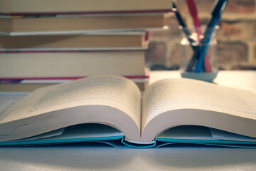 An open book on a desk, in the background a pile of books and a pen holder, warm light coming from a window, concept 