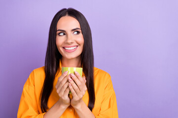 Photo of young dreaming girl wear orange shirt hold cup fresh coffee good flavor look empty space cafe isolated on violet color background