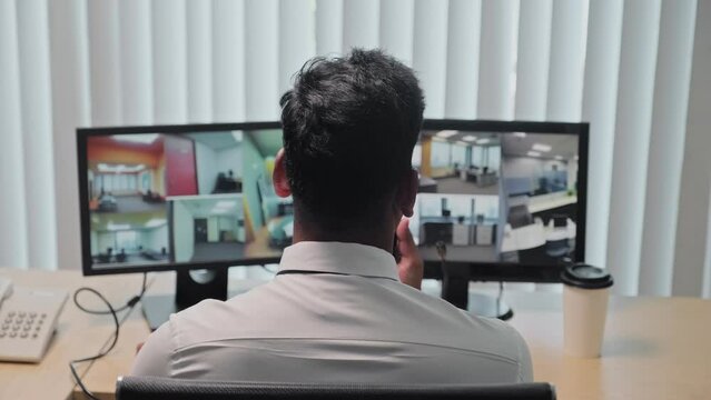 Back view of security guard monitoring surveillance cameras at workplace