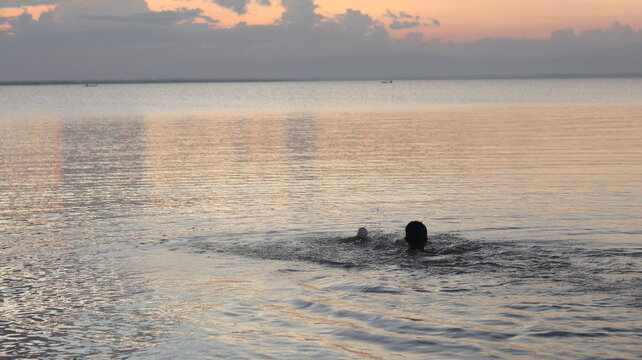 Silhouette of a man swimming in the lake at sunset. - Powered by Adobe