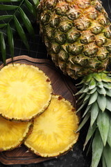 Slices of tasty ripe pineapple and whole fruit on black table, flat lay