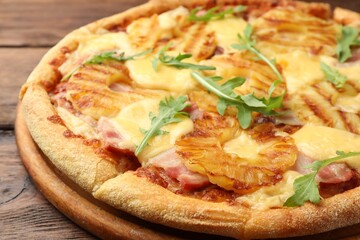 Delicious pineapple pizza with arugula on wooden table, closeup