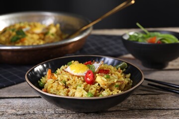 Tasty rice with meat, egg and vegetables in bowl on wooden table