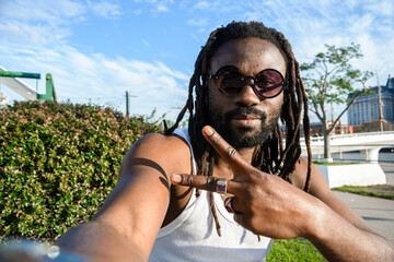 young African man with dreadlocks and beard sitting looking at camera making v sign with hand