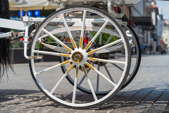 Close-up of large wheels of a white horse-drawn carriage on a sunny day on a cobbled street of an old European city. Retro revival, sustainable development cities. Eco-conscious consumerism