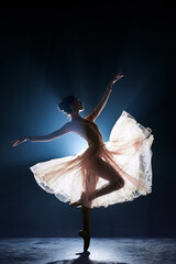 Theatrical performance. Beautiful, tender, graceful ballerina dancing against dark blue background with spotlight