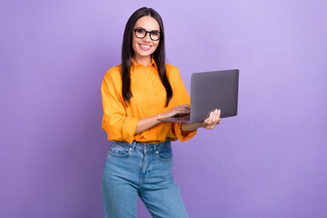 Photo of good mood adorable girl straight hairdo dressed yellow shirt hold laptop typing email isolated on purple color background