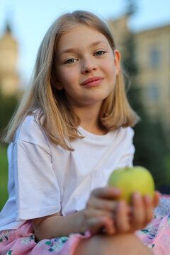 Portrait of a positive girl with an apple in her hands on the background of the school.