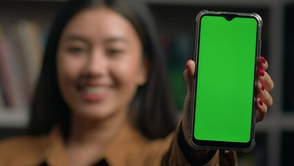 Smiling asian woman girl holding smartphone showing new application close-up green empty screen gadget mobile phone chroma key display mockup digital device advertisement advertise app web service