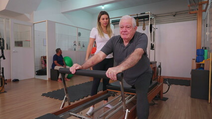 Older man exercising in Pilates studio being oriented by female coach. Senior person taking care of spine health